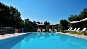 A swimming pool with lounge chairs and umbrellas, surrounded by trees and buildings. - Four Points by Sheraton Siena (Siena)