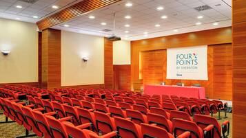 A conference room with rows of red chairs, a podium, and a presentation screen displaying "FOUR POINTS BY SHERATON".