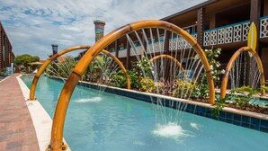 A pool with bamboo arches and water features, surrounded by a building with balconies and a tiled pool edge. - Westgate Cocoa Beach Resort (Cocoa Beach)