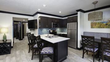 A modern kitchen with dark cabinetry, a central island, and a dining area with chairs.