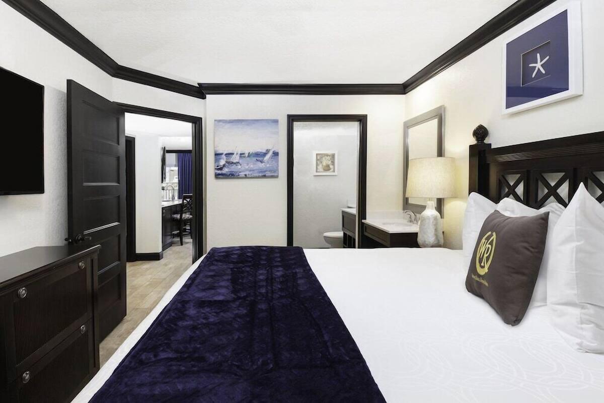 A hotel room with a bed, a desk, a chair, a TV, and a door leading to a bathroom.