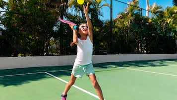 A tennis court with a net, surrounded by palm trees and a clear sky.