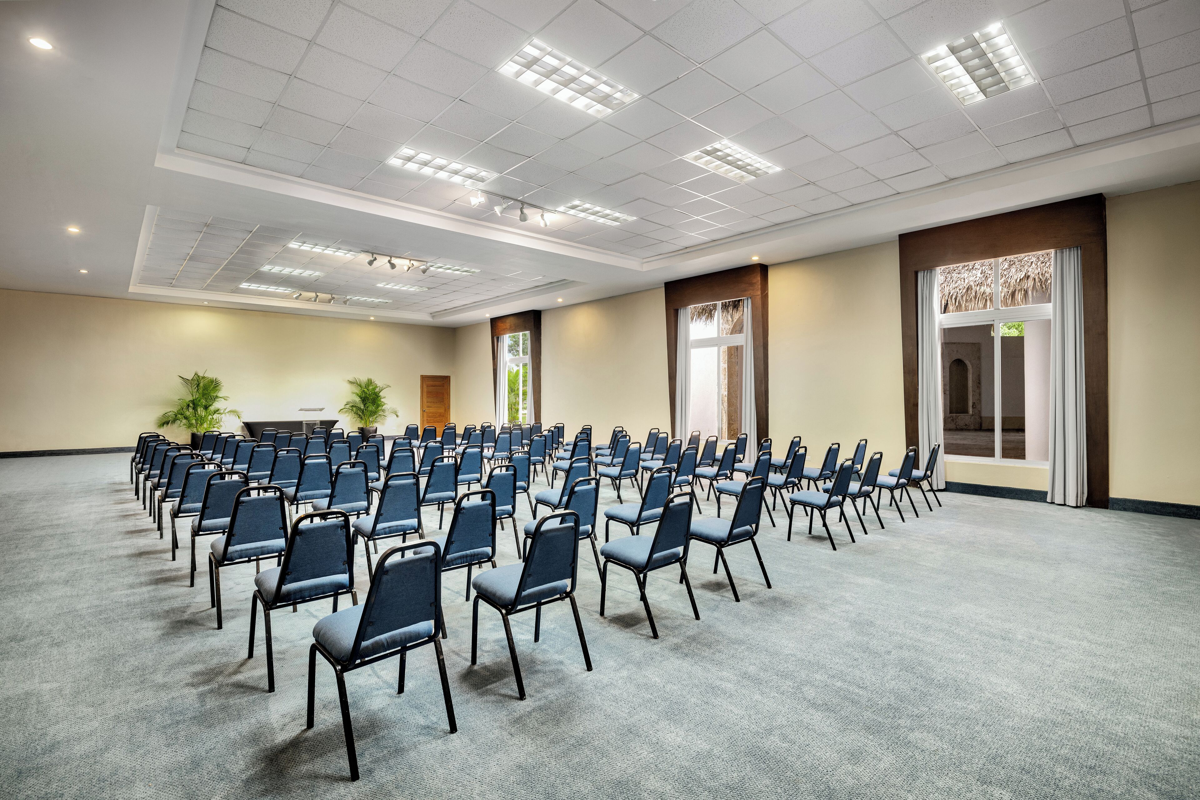 Sala de conferência com fileiras de cadeiras, piso coberto por carpete e teto com iluminação embutida.