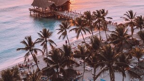 A beach resort with a pier extending into the ocean, palm trees, and beach chairs.