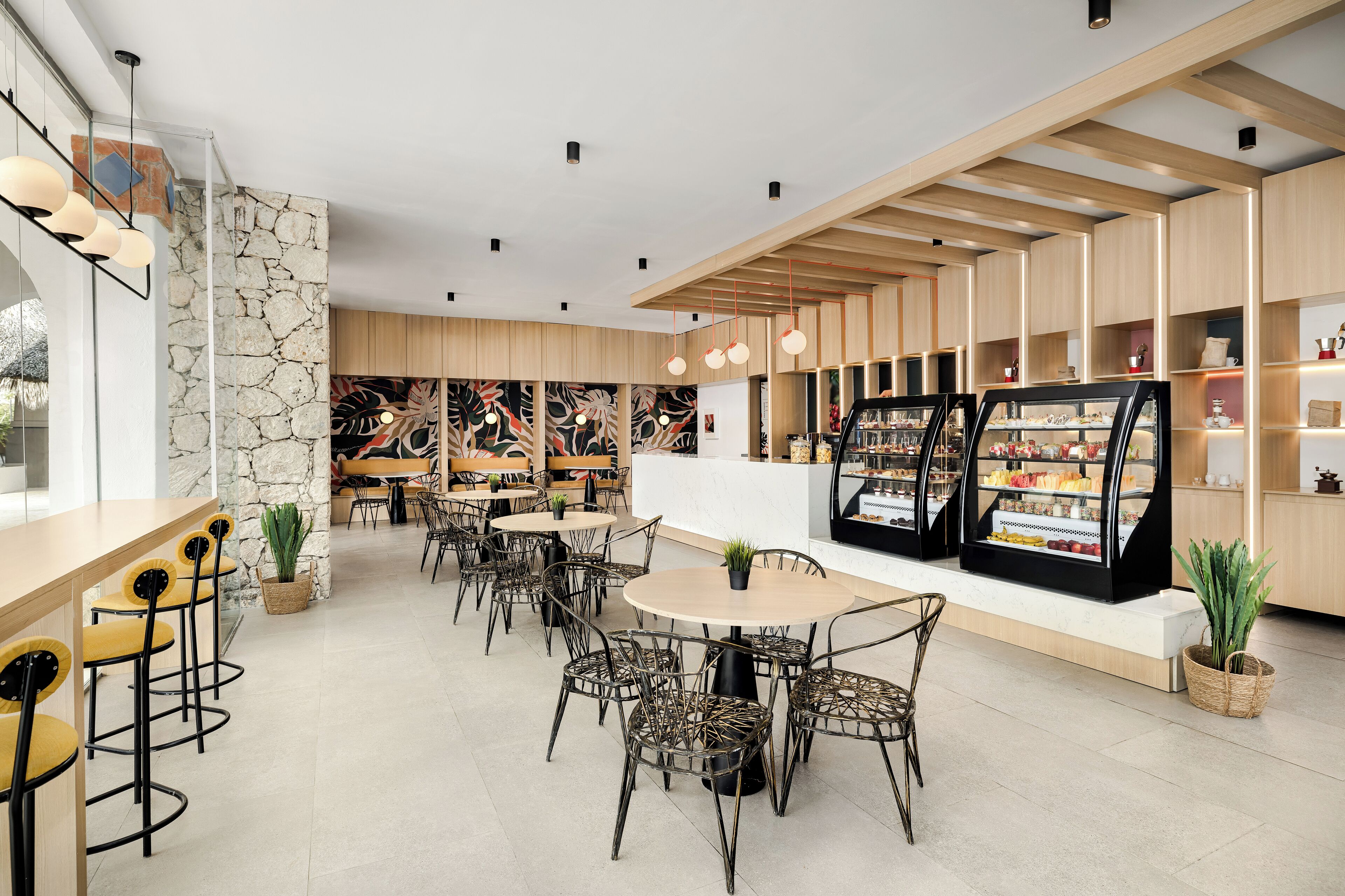 A modern cafe with wooden furniture, a stone accent wall, and a counter with a display case.