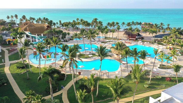 A resort with multiple swimming pools, palm trees, and a beach view.