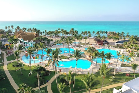 A resort with multiple swimming pools, palm trees, and a beach view.
