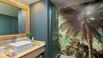 Une salle de bain moderne avec un grand miroir, un lavabo rectangulaire, une douche en verre et une fresque murale représentant des palmiers.