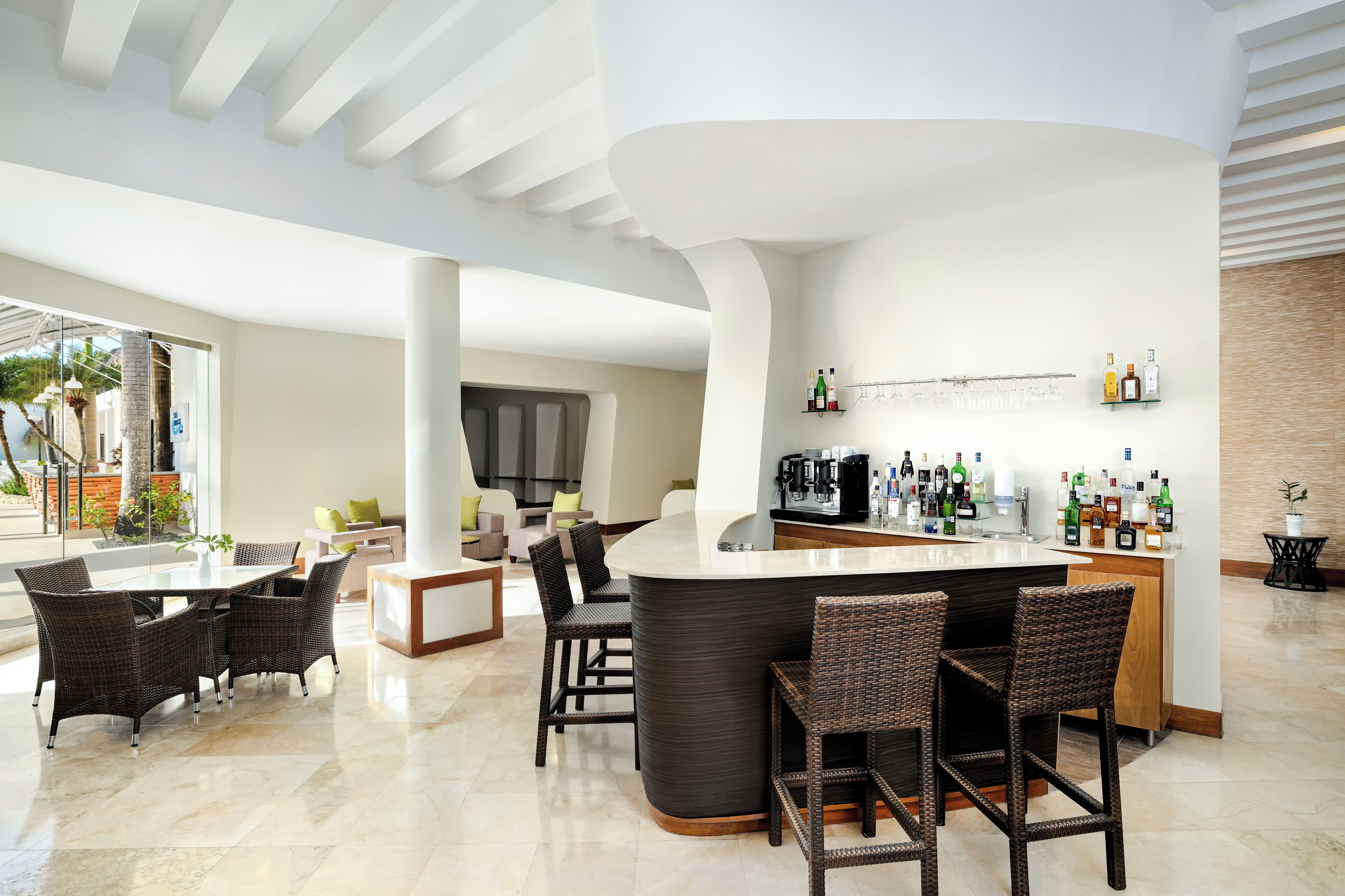 A modern bar area with a curved counter, wicker chairs, and a variety of liquor bottles.