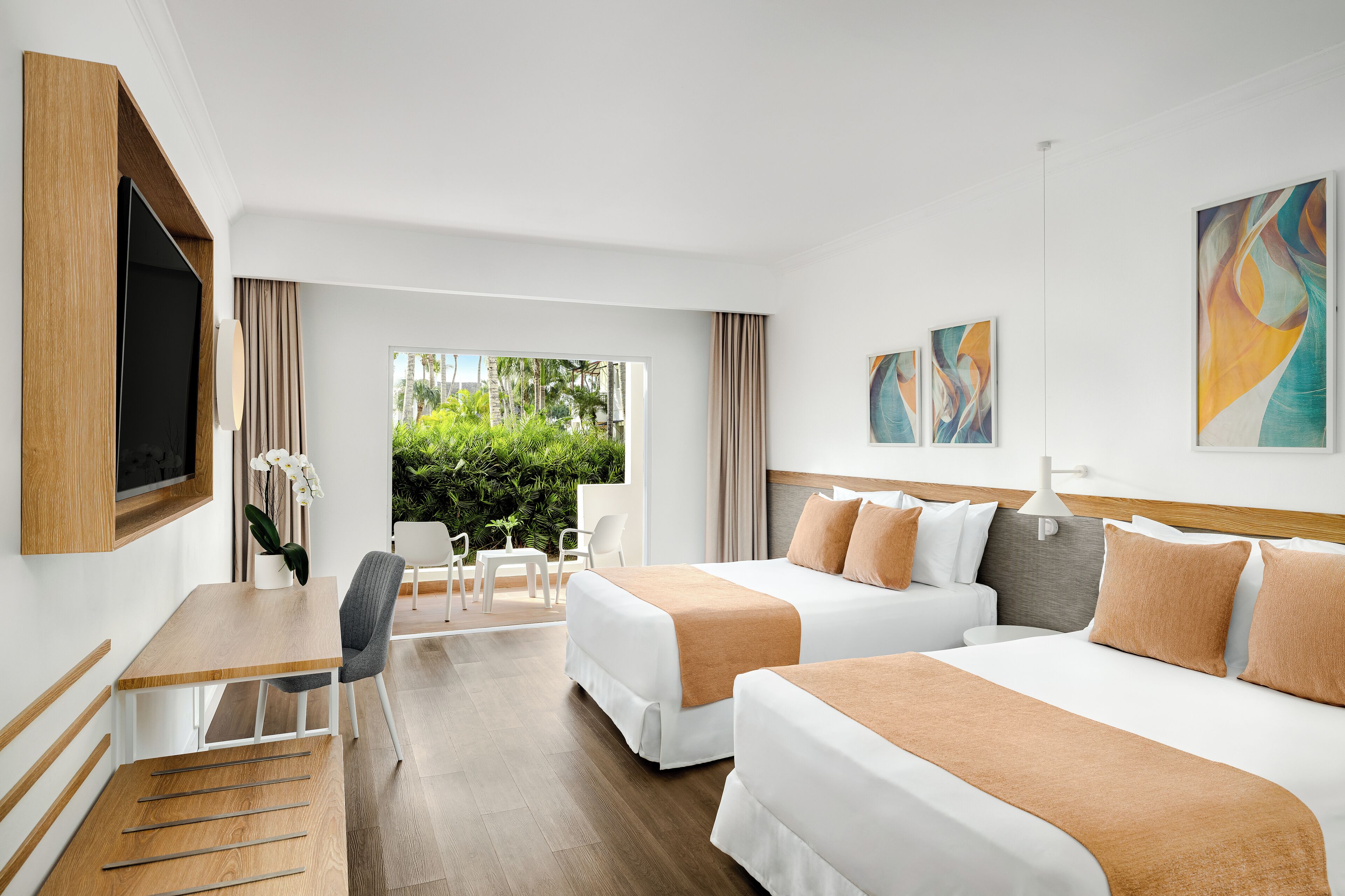 Habitación de hotel con dos camas, un escritorio con silla, televisión y obras de arte en las paredes.