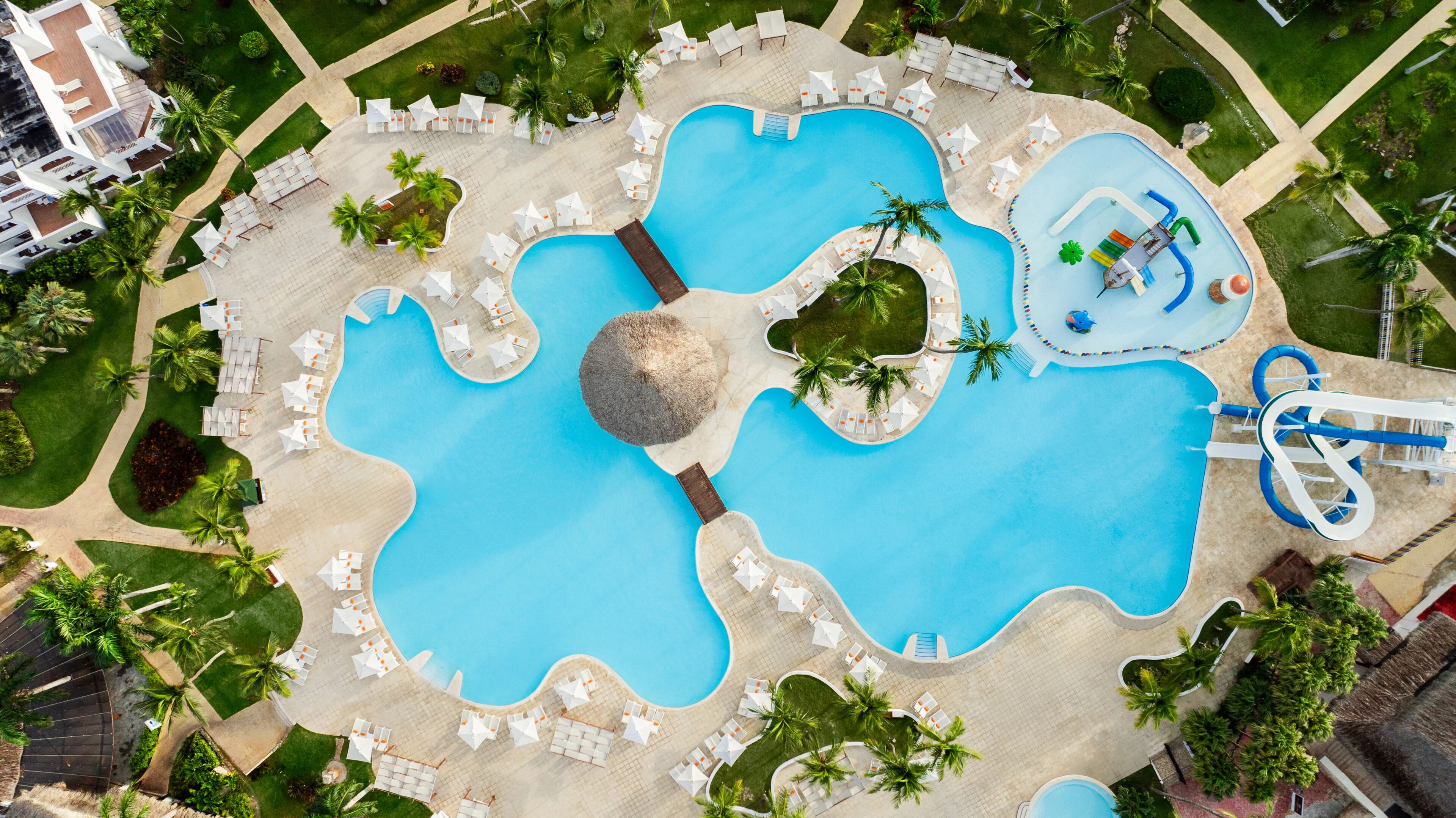 Vue aérienne d’un complexe hôtelier doté de plusieurs piscines, de chaises longues et de palmiers.