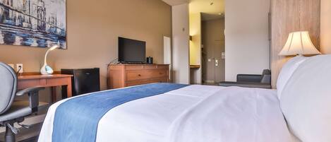 Habitación de hotel con cama, escritorio, silla, lámpara y un cuadro en la pared.