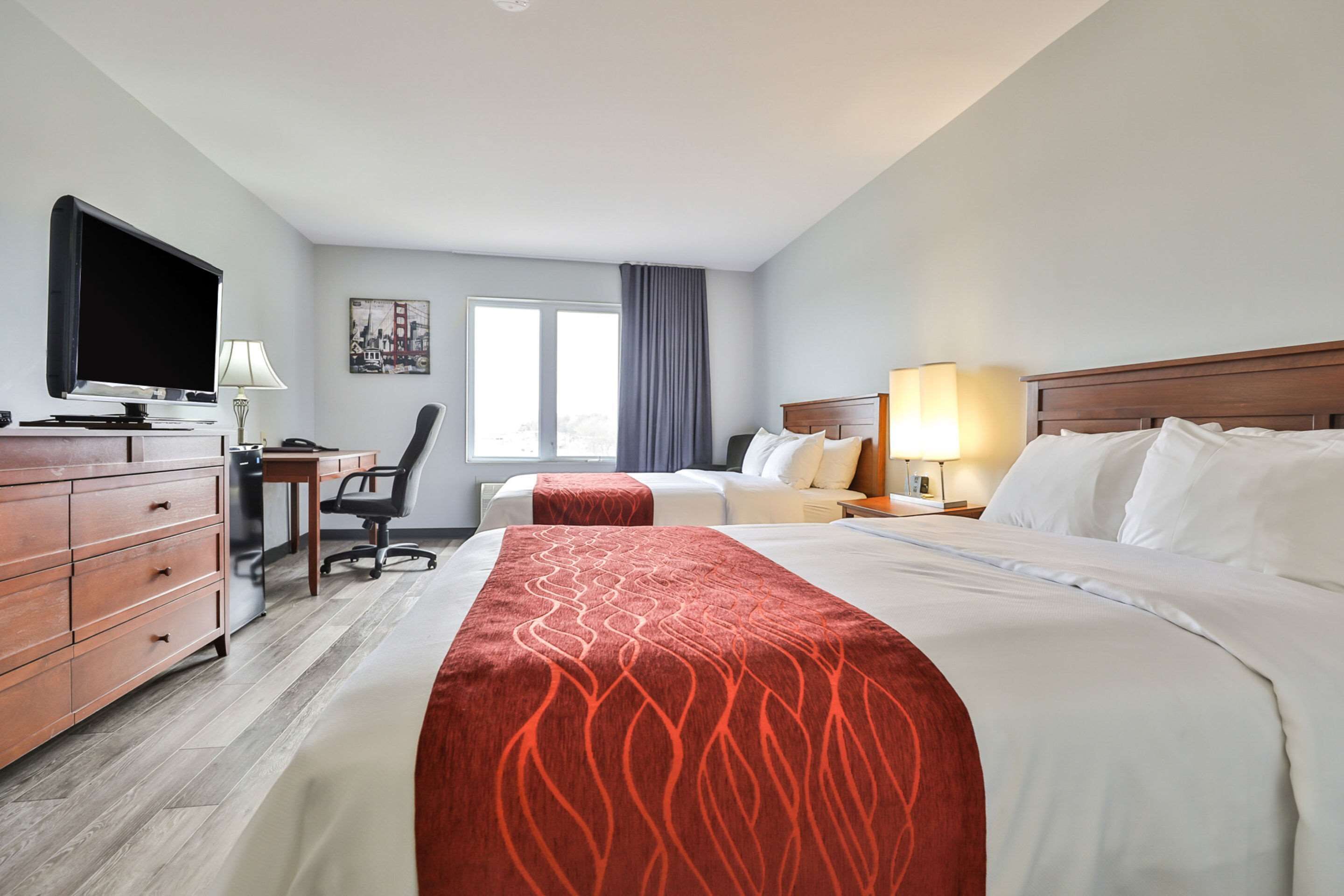A hotel room with two beds, a desk with a computer, a TV, and a window with curtains.