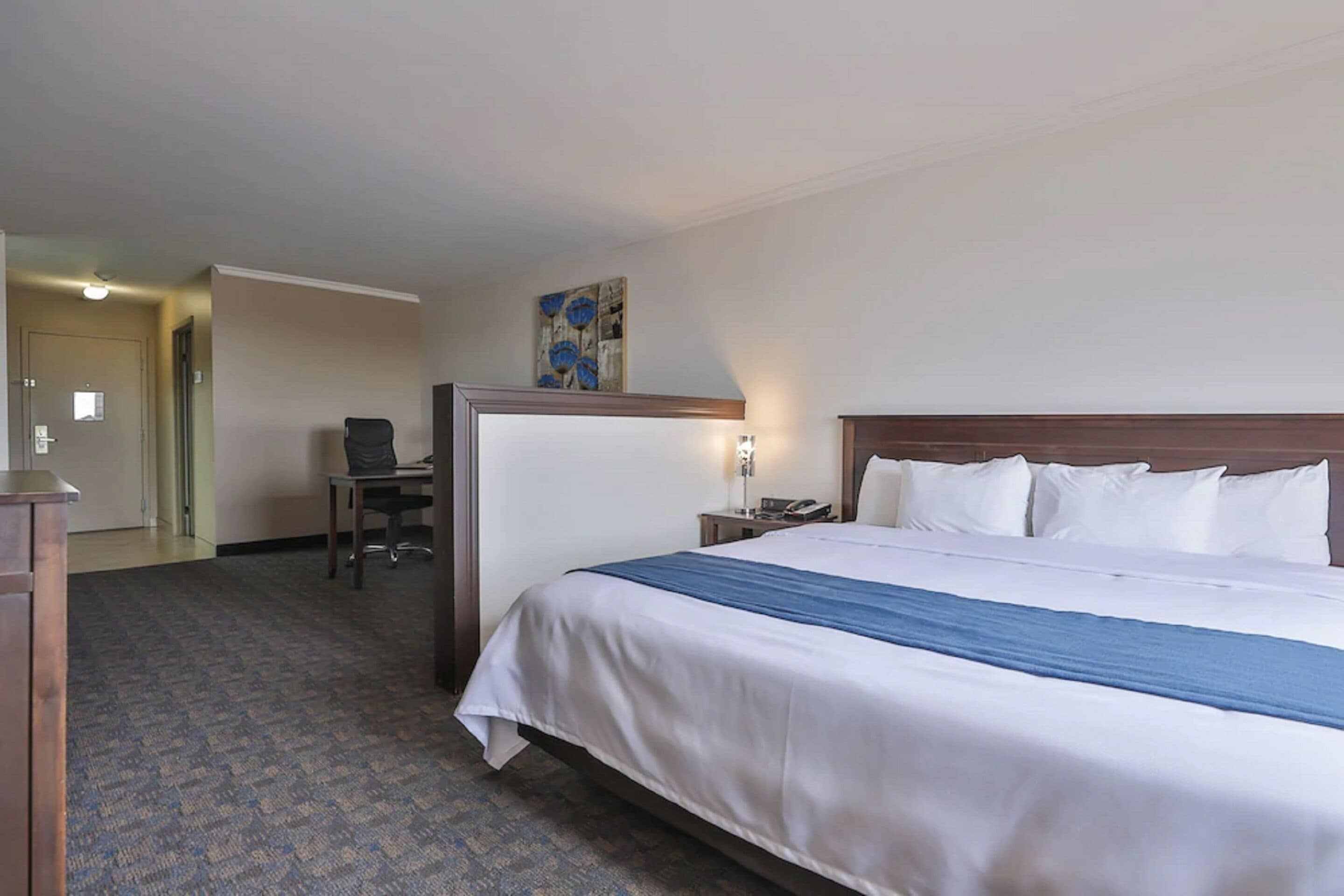 Een hotelkamer met een groot bed, een bureau met stoel, een nachtkastje met lamp en een schilderij aan de muur.