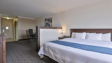 Een hotelkamer met een groot bed, een bureau met stoel, een nachtkastje met lamp en een schilderij aan de muur.
