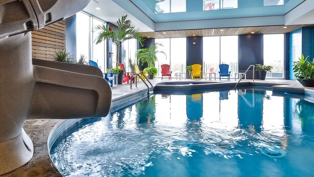 Un espace piscine intérieur moderne, doté d'un plafond en verre transparent, de plusieurs chaises longues et de plantes en pot.