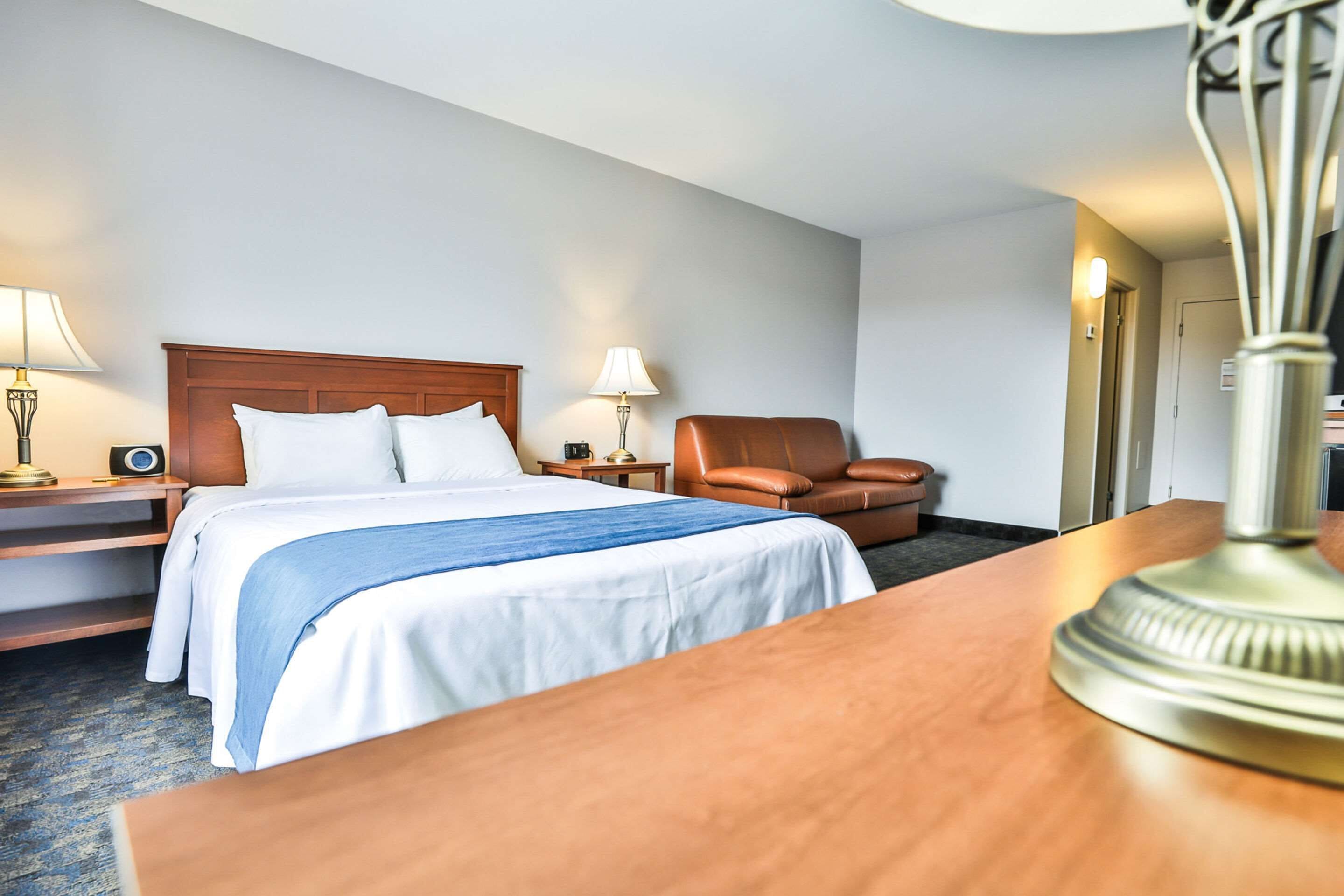 A hotel room with a bed, a chair, a desk, and a lamp.