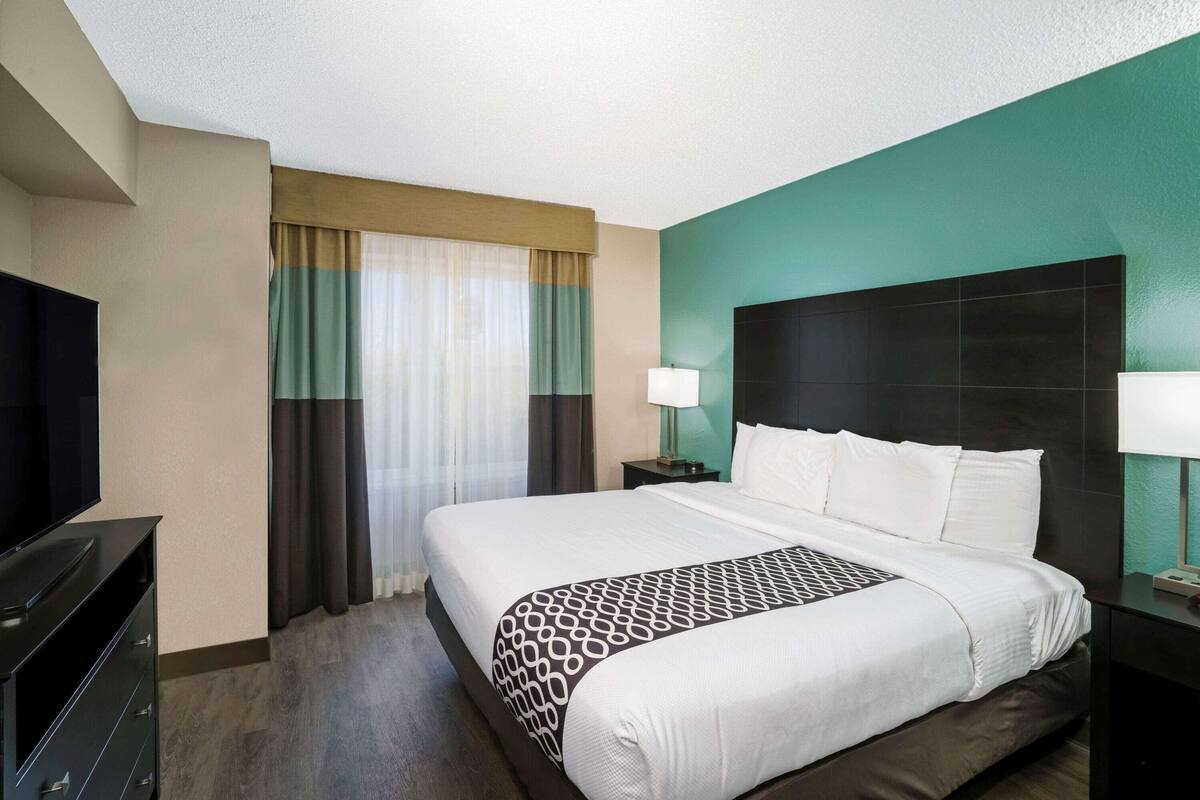 Une chambre d’hôtel avec un grand lit, une télévision, une table de chevet avec une lampe et une fenêtre avec des rideaux.