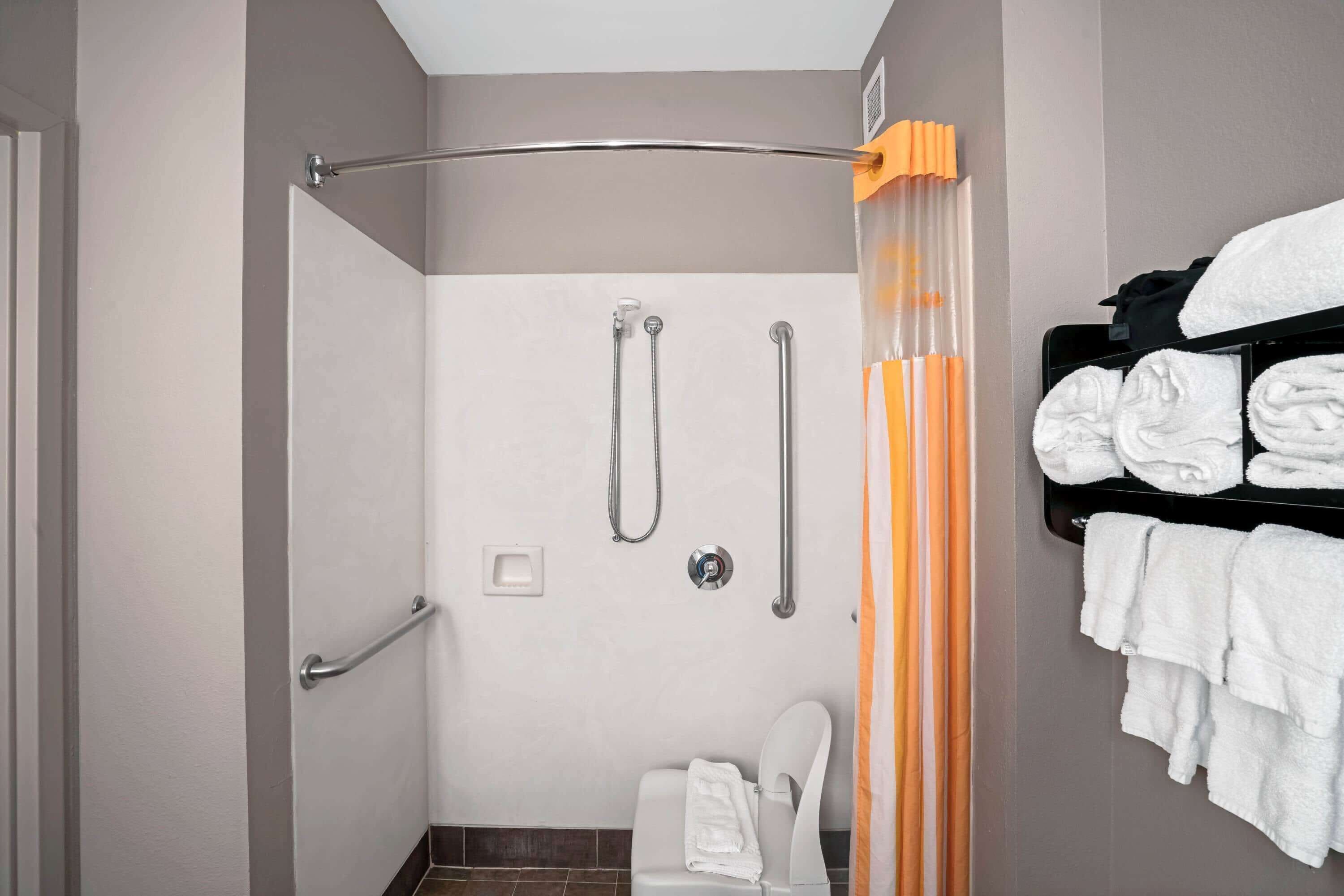 A shower with a grab bar, a white toilet, and a towel rack with folded towels.