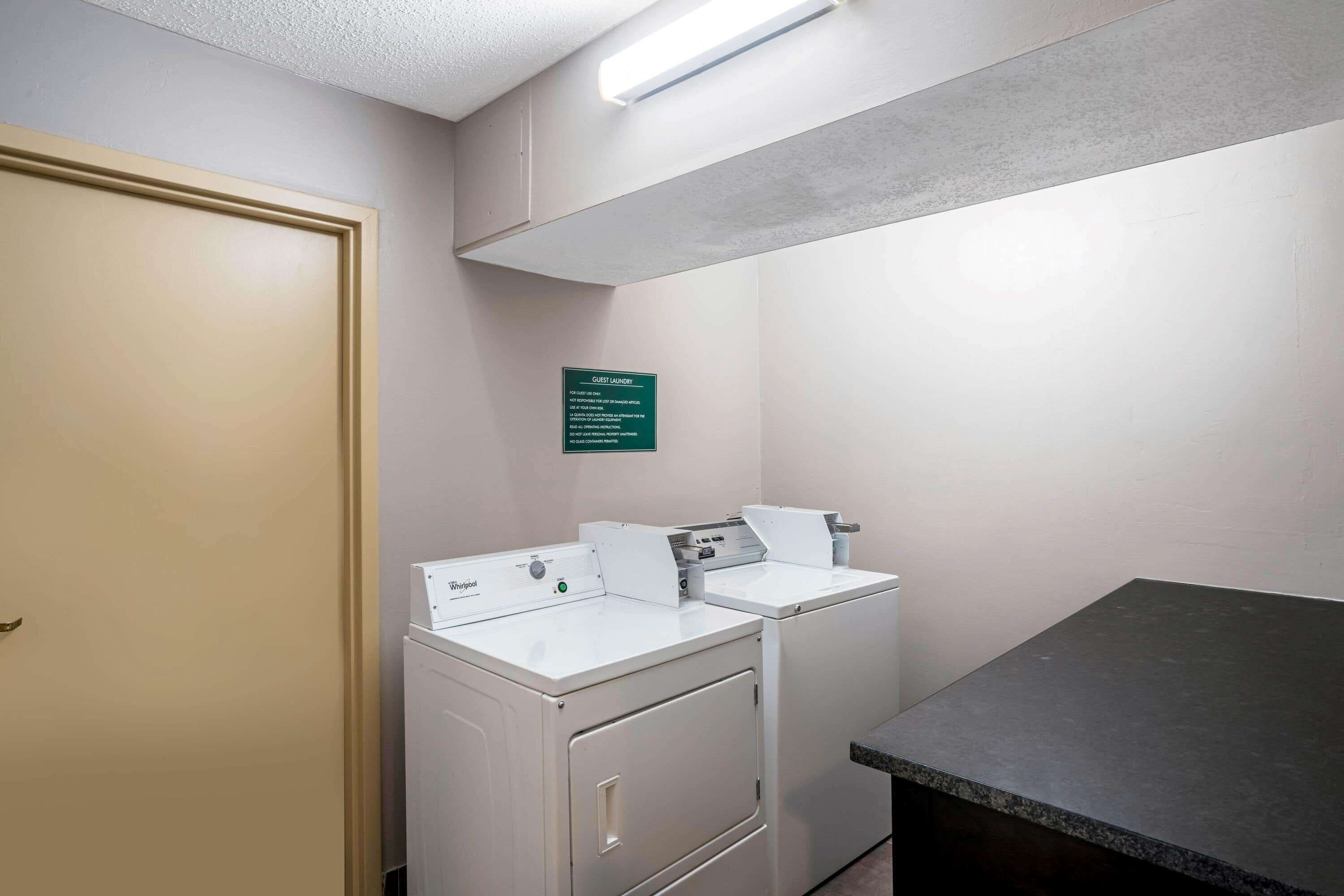 A laundry room with two white Whirlpool washers and dryers, a green sign, and a dark countertop.