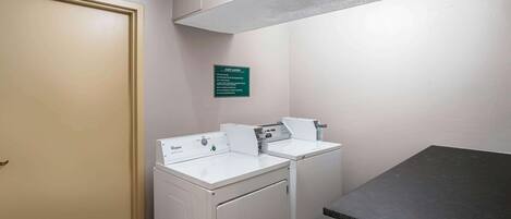 A laundry room with two white Whirlpool washers and dryers, a green sign, and a dark countertop.