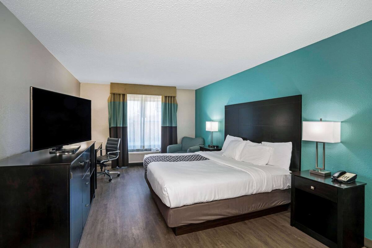 Une chambre d’hôtel avec un lit, un bureau, une télévision et une fenêtre avec des rideaux.