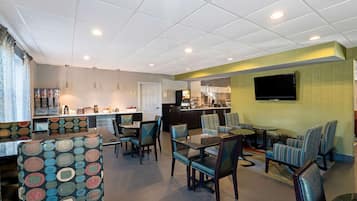 A hotel lobby with a dining area, a kitchen, and a TV mounted on the wall.