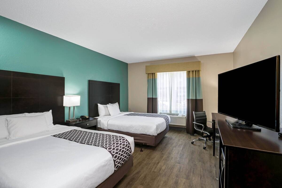 Une chambre d’hôtel avec deux lits, un bureau, une télévision et une fenêtre avec des rideaux.