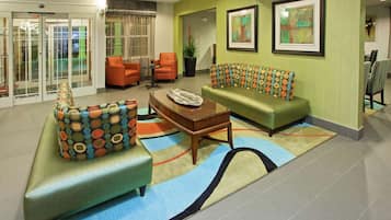 A lobby with green sofas, orange chairs, a wooden coffee table, and a patterned ottoman.