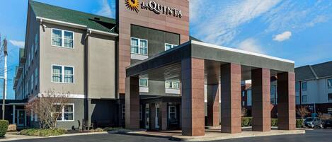 Un hotel con un llamativo letrero de 'La Quinta', un acceso cubierto y un estacionamiento.
