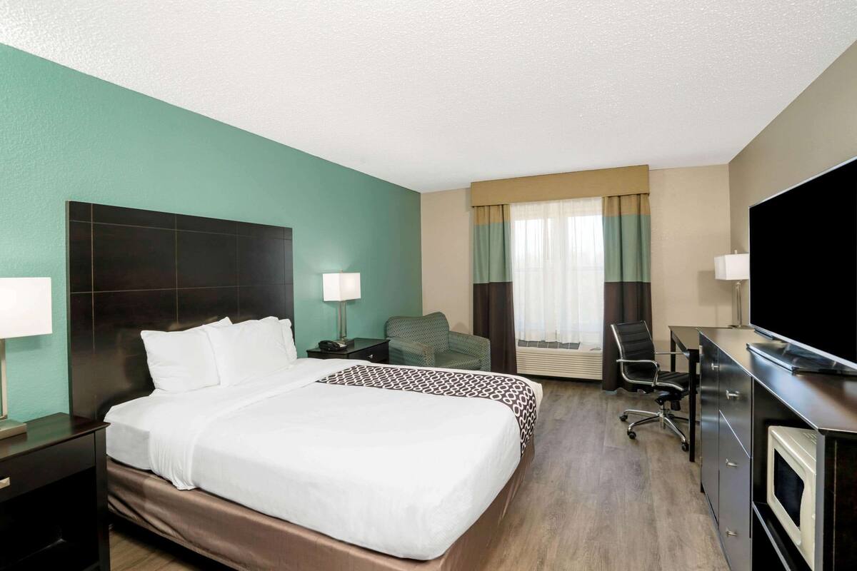 Une chambre d’hôtel avec un grand lit, un bureau, une chaise, une télévision et une fenêtre avec des rideaux.