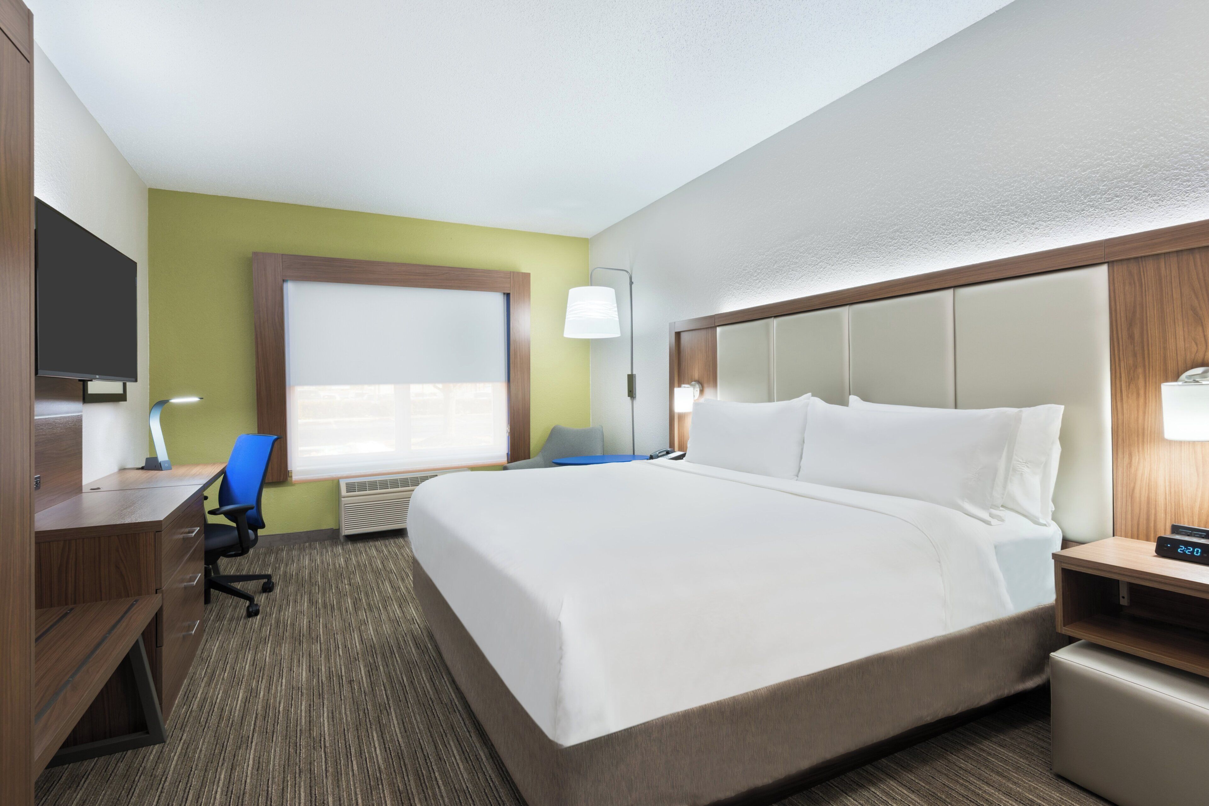 A hotel room with a bed, desk, chair, and a television.