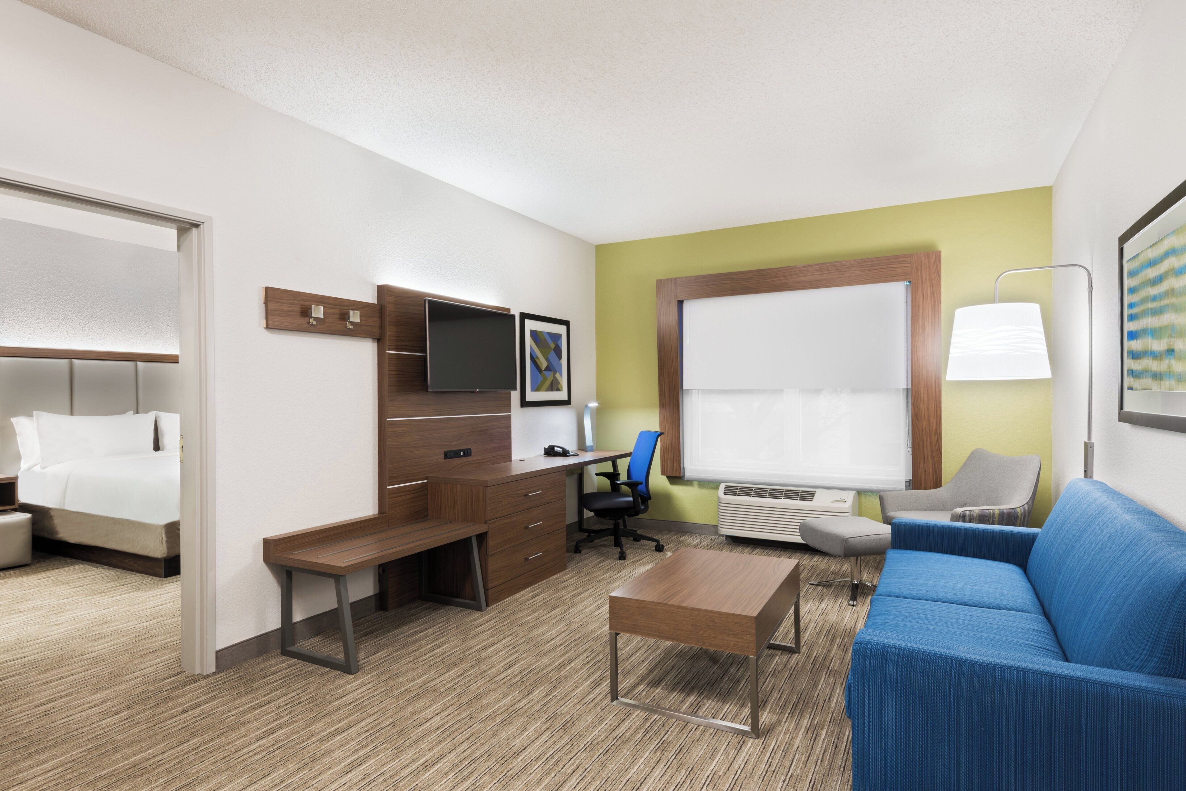 Habitación de hotel con cama, escritorio, silla, sofá y un ventanal amplio.