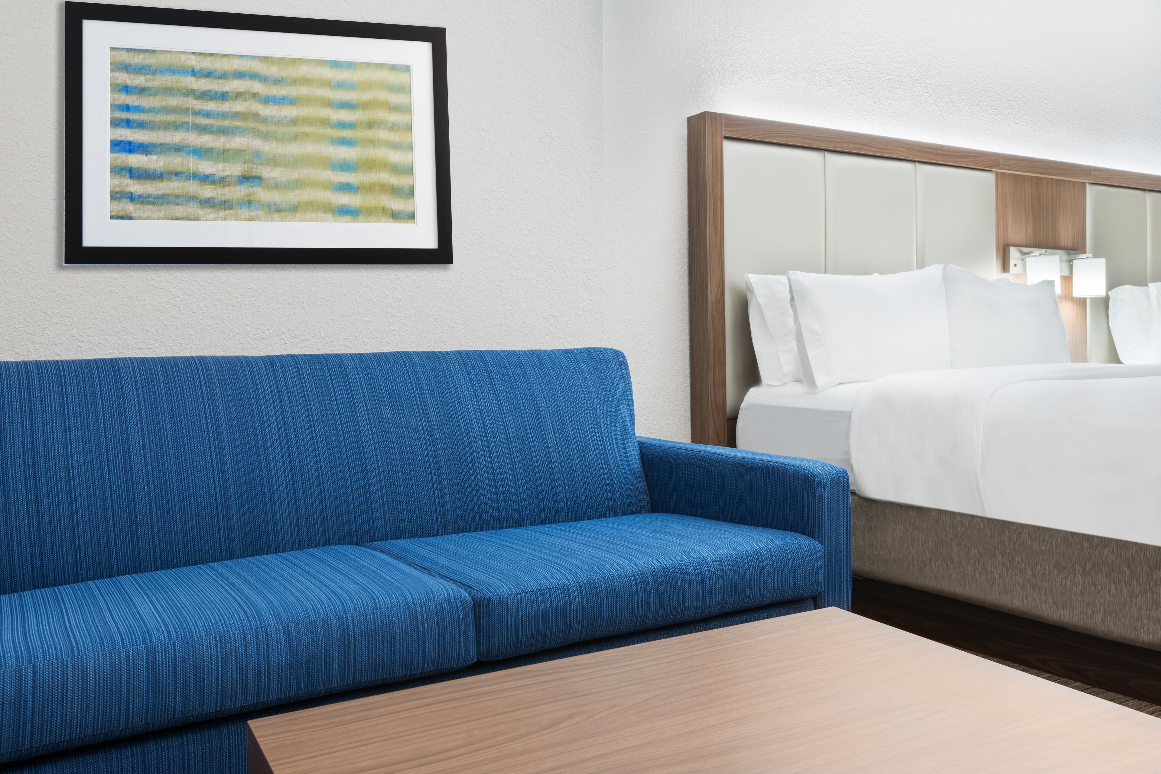 A hotel room with a blue sofa, a wooden table, and a bed with white bedding.