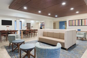 A modern lounge area with a sofa, chairs, a coffee station, and a flat-screen TV. - Holiday Inn Express & Suites Columbus Airport East by IHG (Columbus)