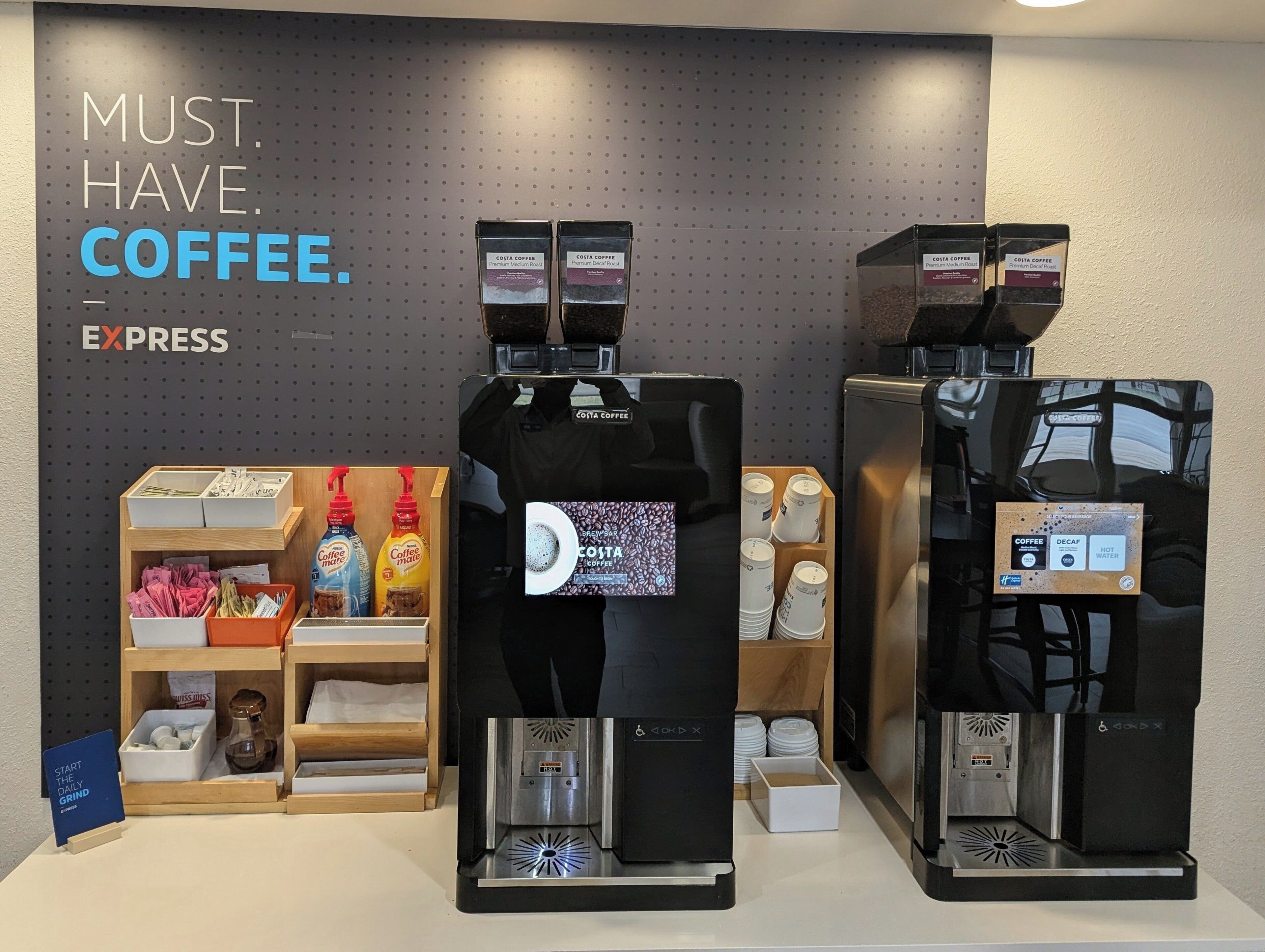 Un espace dédié au café, équipé de deux machines à expresso, d’une pancarte indiquant « CAFÉ EXPRESS OBLIGATOIRE » et de divers accessoires liés au café.