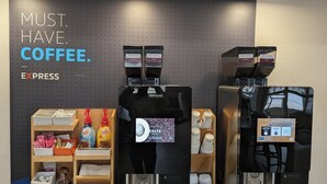 A coffee station with two espresso machines, a sign reading "MUST. HAVE. COFFEE. EXPRESS", and various coffee-related items. - Holiday Inn Express & Suites Columbus Airport East by IHG (Columbus)