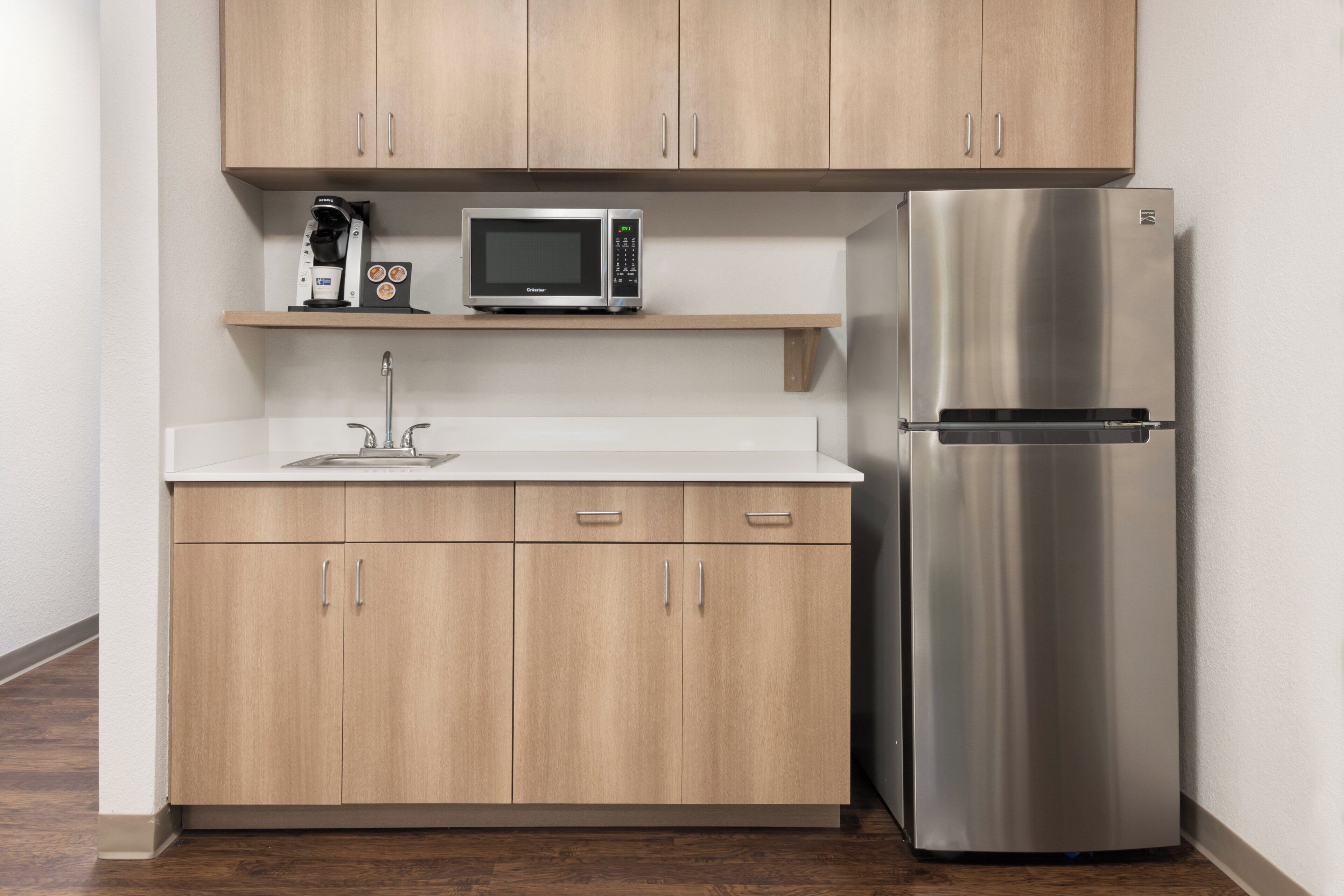 Una cocina compacta con un refrigerador de acero inoxidable, un microondas y una cafetera en un estante.