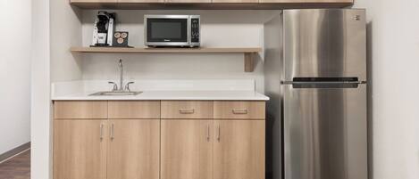 Una cocina compacta con un refrigerador de acero inoxidable, un microondas y una cafetera en un estante.