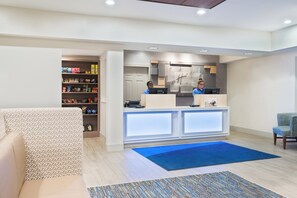 A hotel lobby with a reception desk, a seating area with a patterned sofa, and a snack shelf. - Holiday Inn Express & Suites Columbus Airport East by IHG (Columbus)