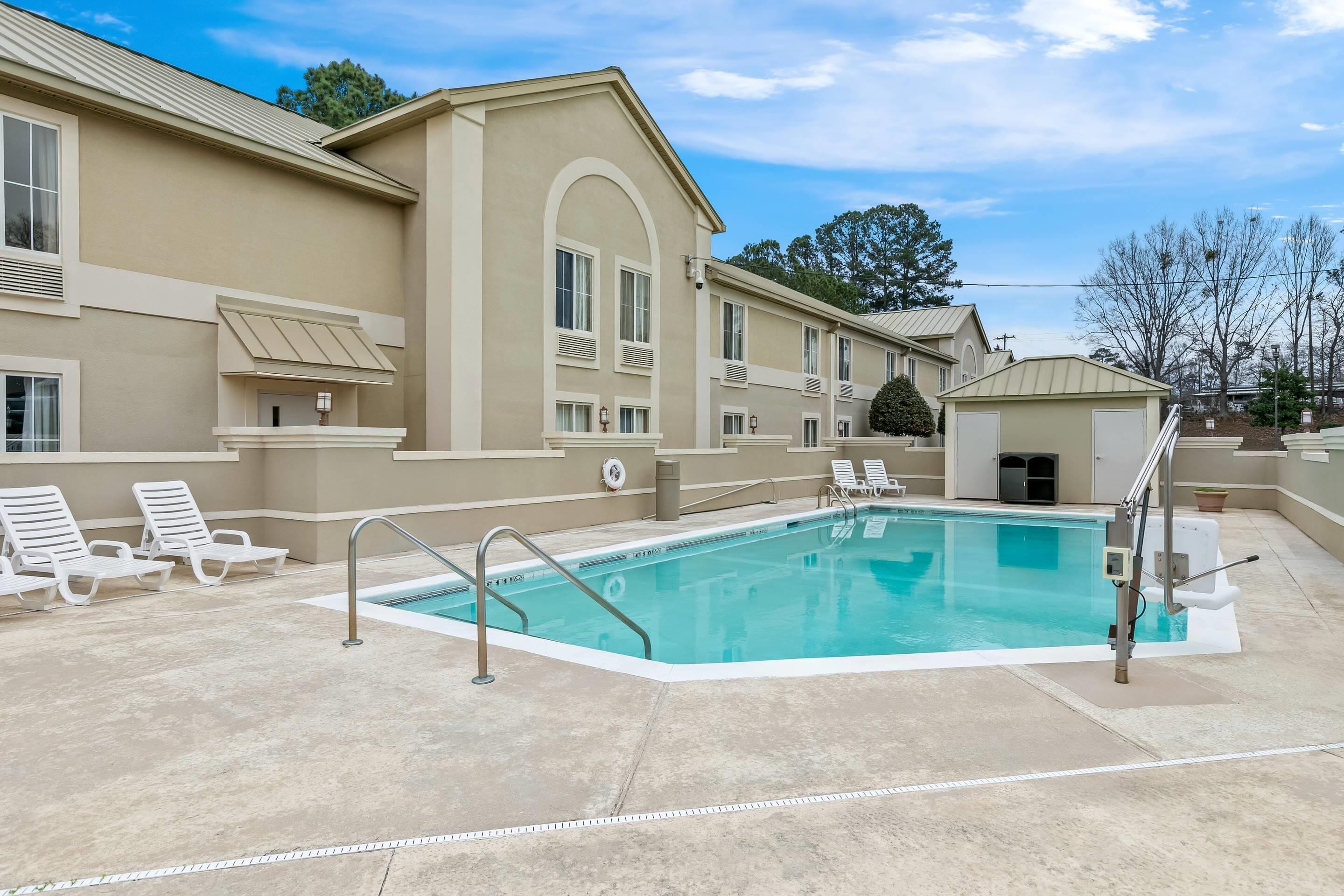 Una piscina con sillones de descanso, un área de estar techada y un edificio de fachada color beige.