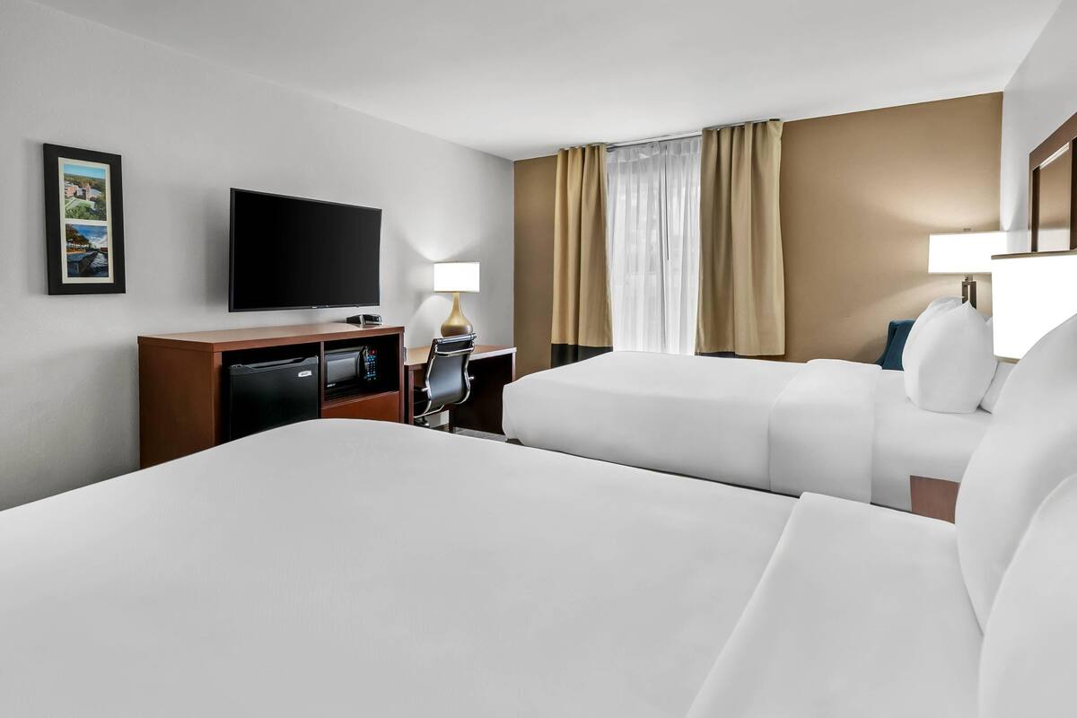A hotel room with two beds, a TV, a desk with a lamp, and a picture on the wall.