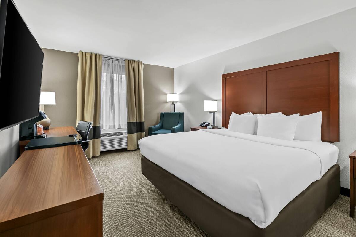 A hotel room with a large bed, a desk, a chair, a TV, and a window with curtains.