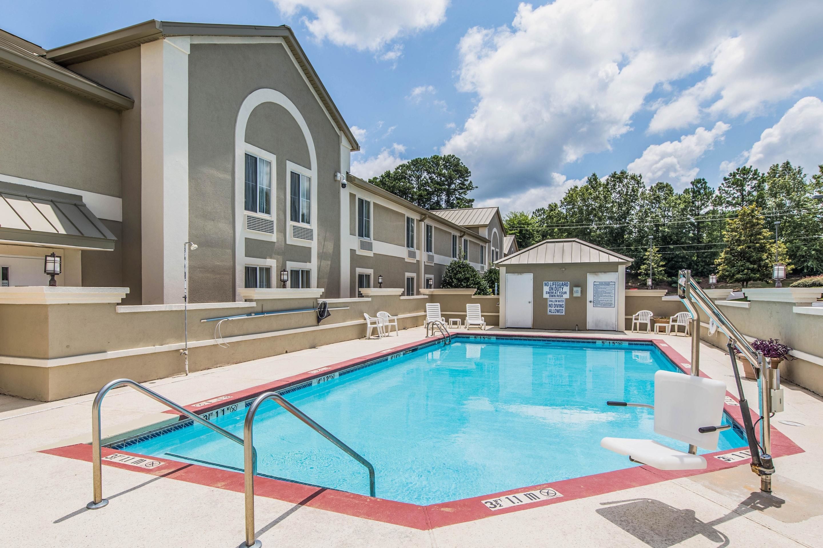 A swimming pool with a lifeguard station, lounge chairs, and a small building with a sign.
