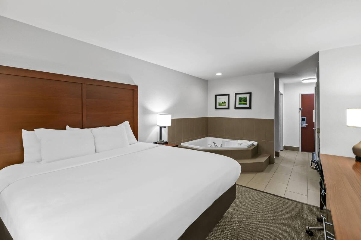A hotel room with a large bed, a bathroom with a bathtub, and a desk with a lamp.