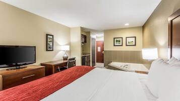 Quarto de hotel com cama, escrivaninha com televisão, banheiro com banheira e cozinha compacta.
