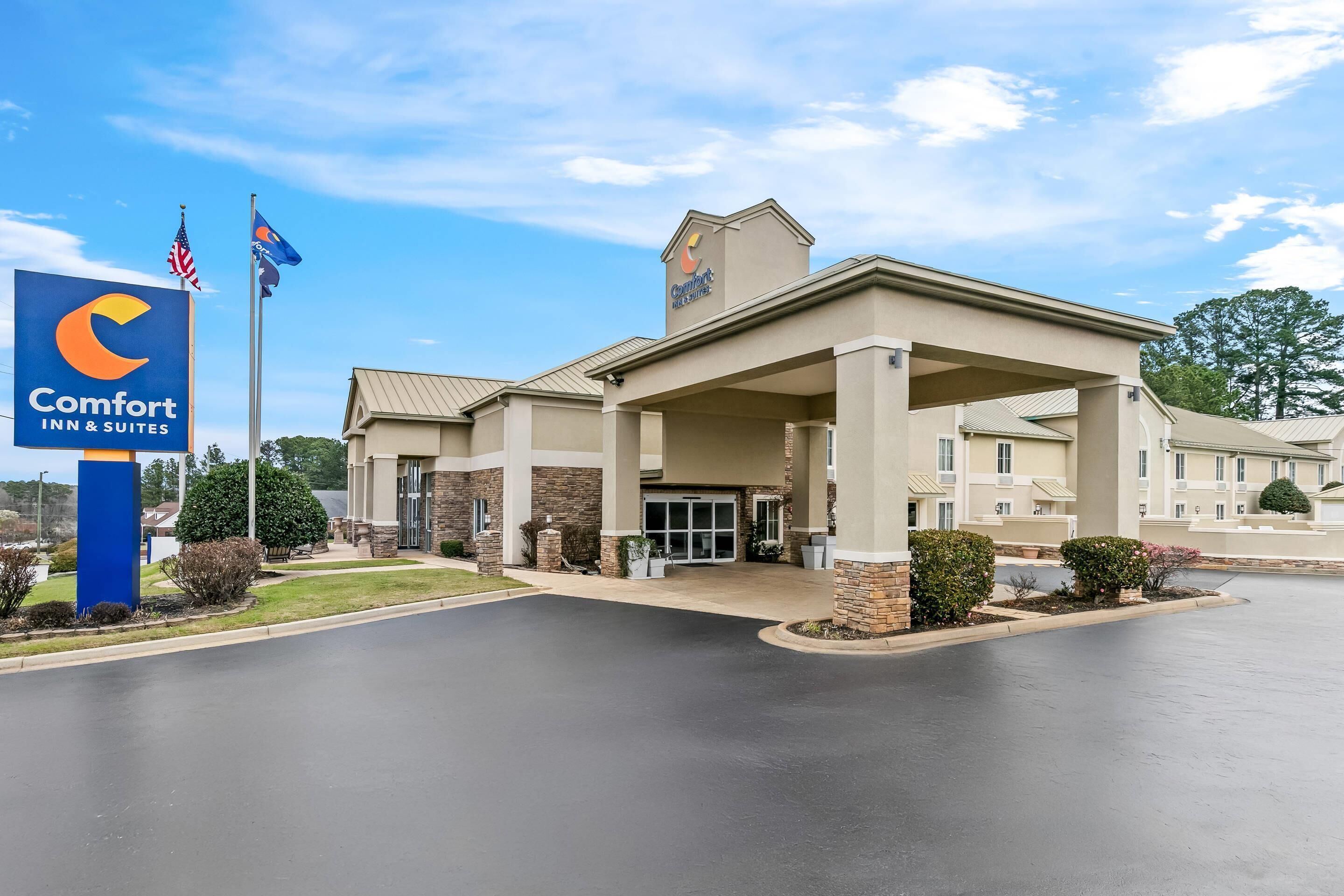 Un Comfort Inn & Suites con entrada despejada, bandera estadounidense y césped bien cuidado.