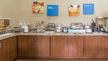 A breakfast area with a granite countertop, coffee machines, a waffle maker, and a bread display.