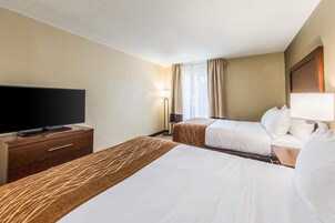 Habitación de hotel con dos camas, un televisor de pantalla plana sobre una cómoda de madera, una lámpara y una ventana con cortinas.