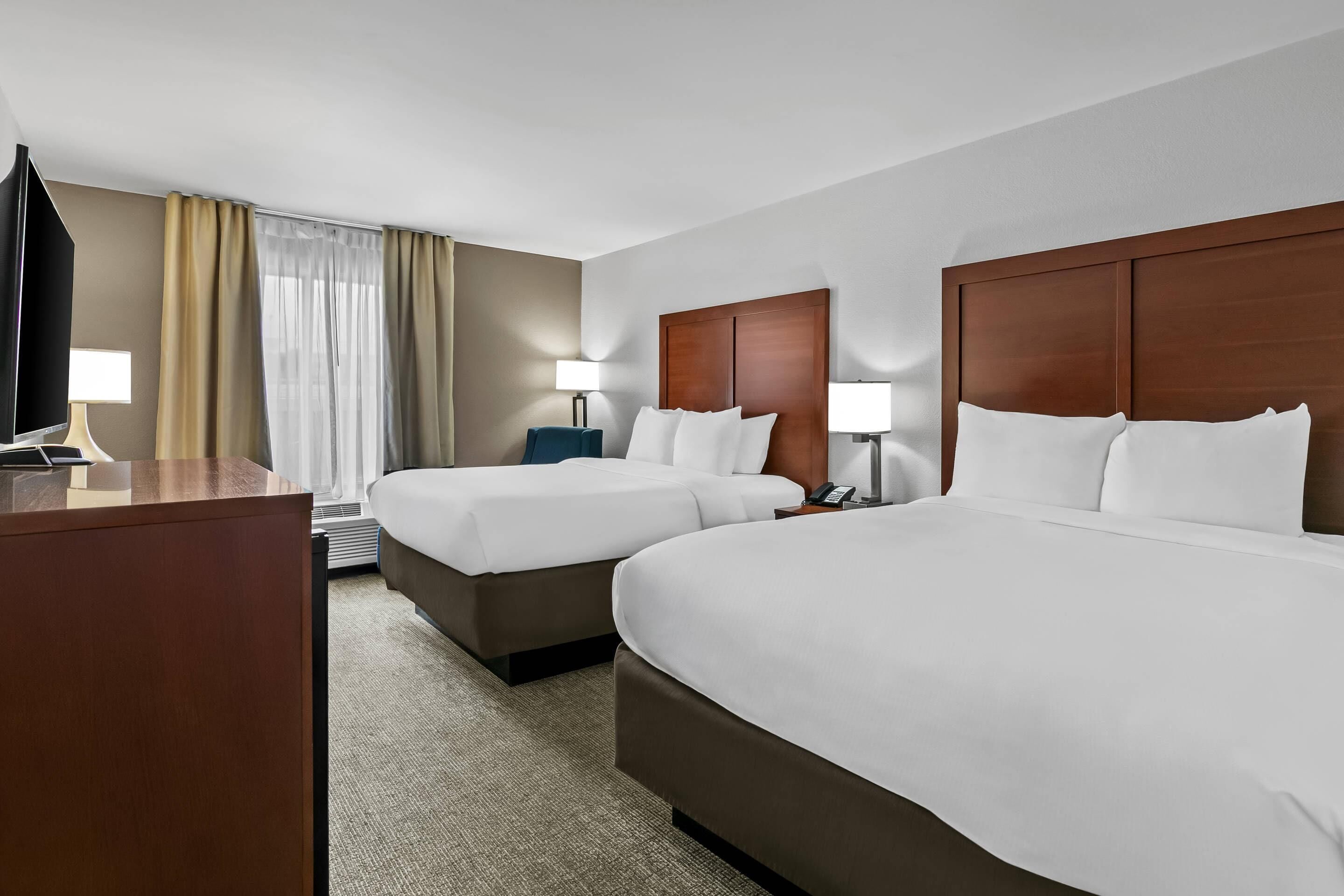 A hotel room with two beds, a desk, a TV, and a lamp.
